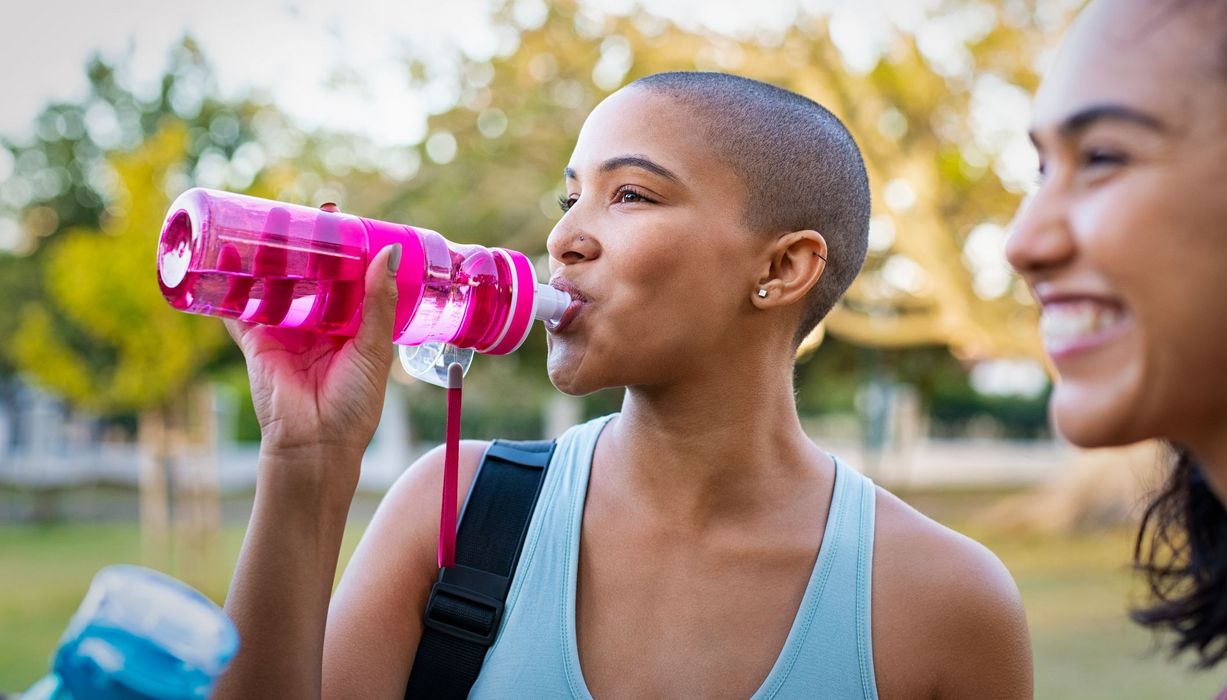 Junge, dunkelhäutige, sportliche Frau, trinkt aus pinker Flasche.