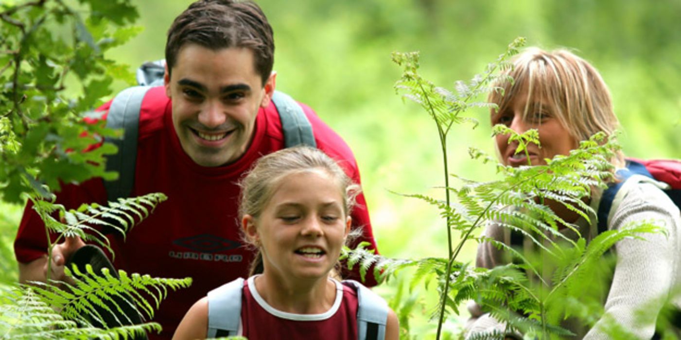 Familie: Mutter, Vater, Tochter, ca. 11 Jahre, mit Rucksäcken beim Wandern querfeldein durch sehr hohes Farnkraut