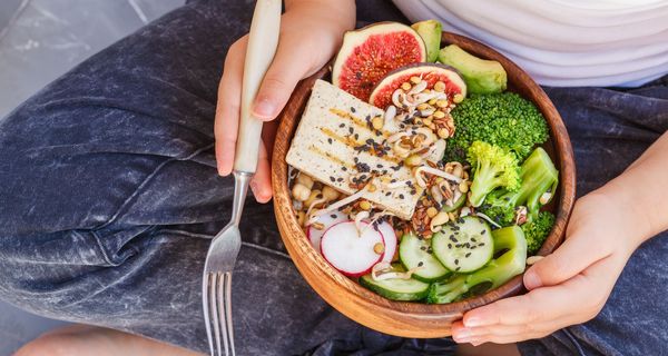 Bowl mit Gemüse und Tofu in den Händen eines Kinds.