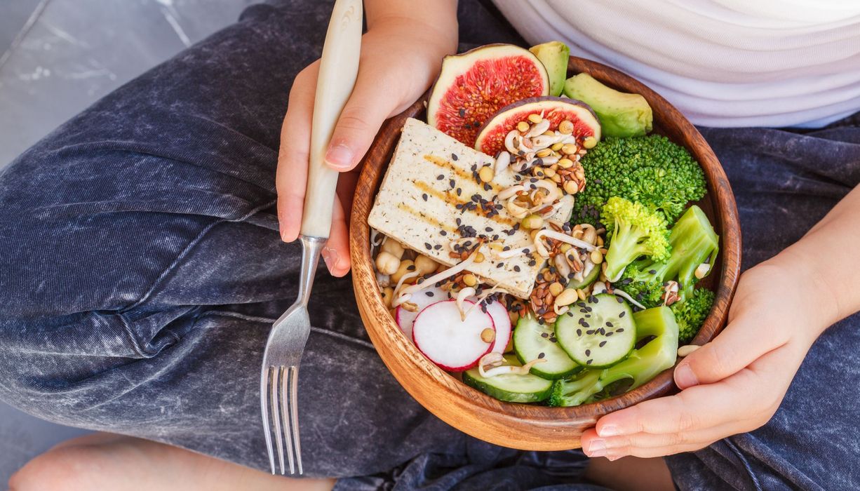 Bowl mit Gemüse und Tofu in den Händen eines Kinds.