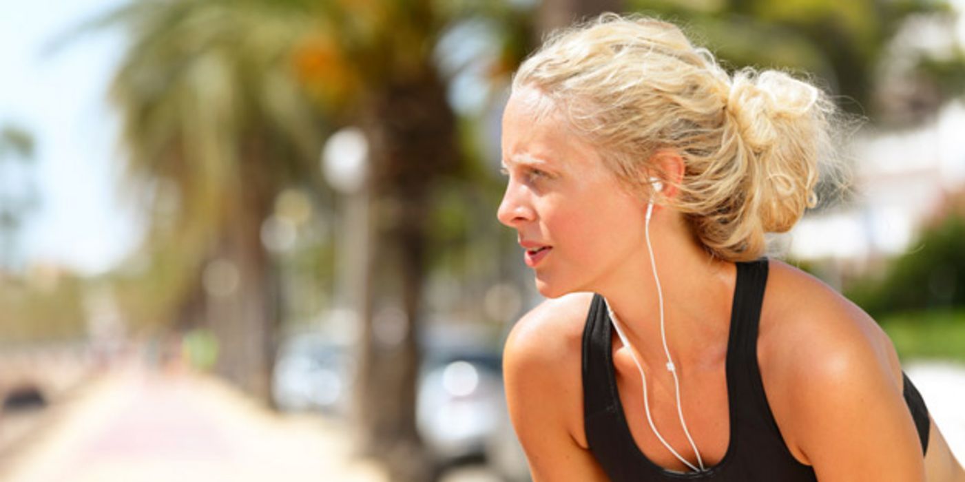 Junge blonde Frau mit Kopfhörern an einem heißen Sommertag, macht eine Pause vom Joggen.