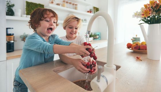 Glückliche Kinder waschen Kirschen unter Leitungswasser in der Küche