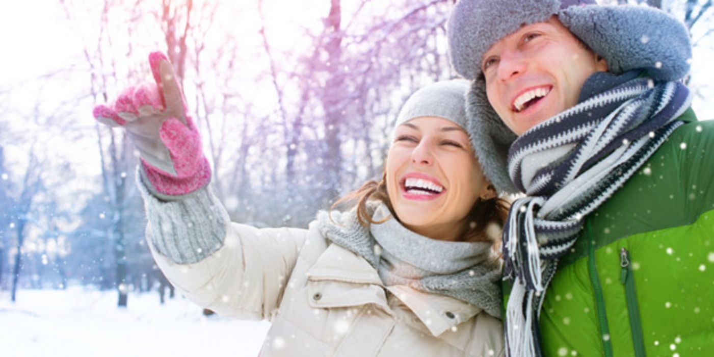 Vergnügtes Paar in winterlicher Landschaft (in den 20ern: Er grüner Anorak und Fellmütze mit Ohrenklappen, sie heller Anorak, rosa Handschuhe, hellgraue Mütze und Schal)