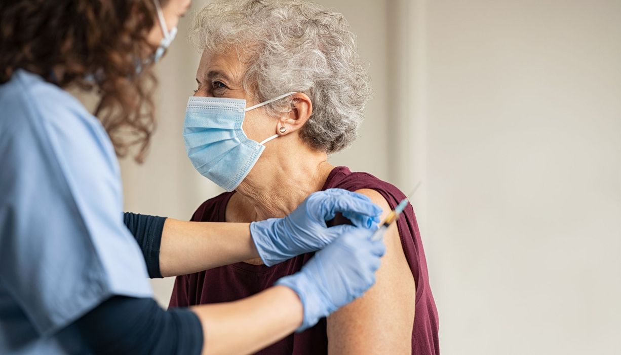 Seniorin mit Maske, wird von Ärztin geimpft.