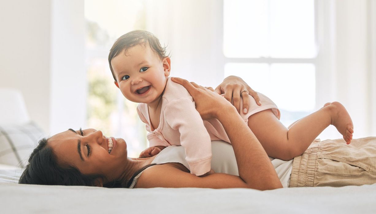 Junge Mutter spielt mit Baby im Bett.