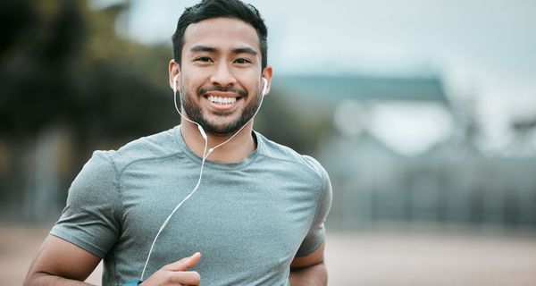 Junger Mann, joggt und lächelt in die Kamera.