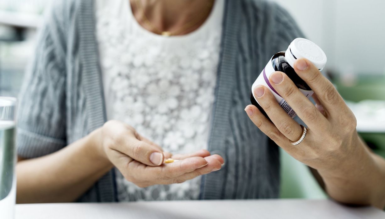 Frau, hält eine Dose mit Tabletten und eine Tablette in der Hand.