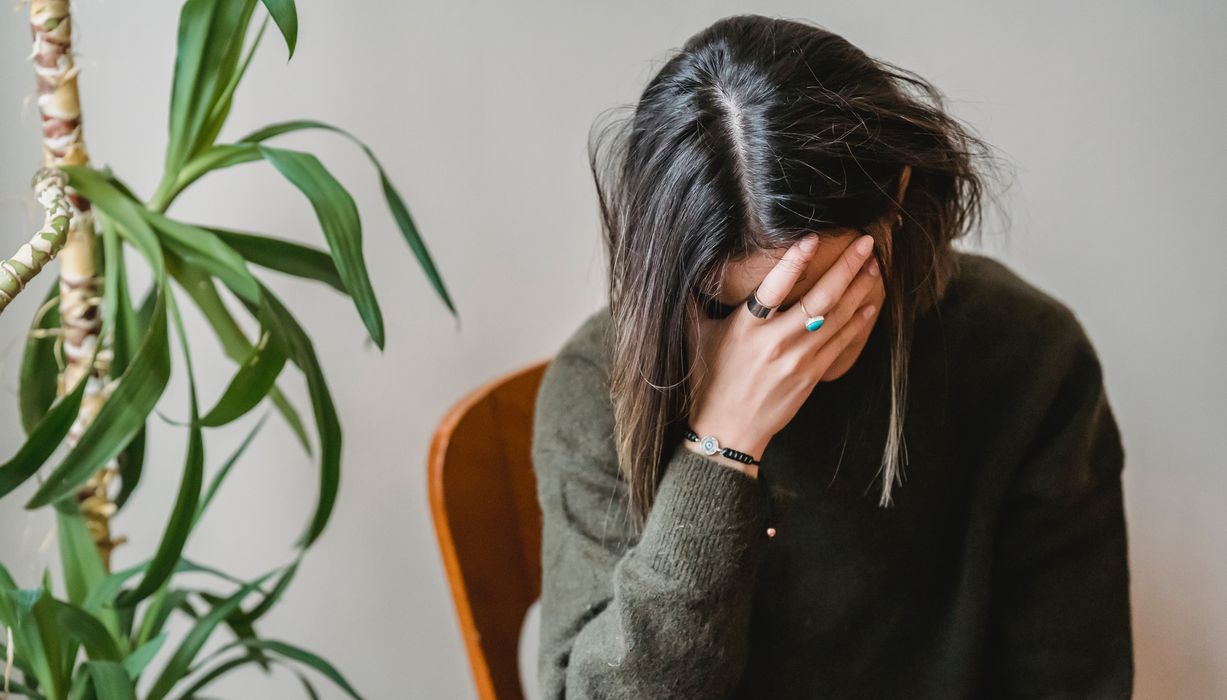 Junge dunkelhaarige Frau, verdeckt ihr Gesicht mit den Händen.