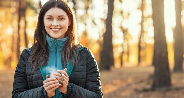 Junge Frau im Wald trinkt eine Tasse dampfenden Tee.