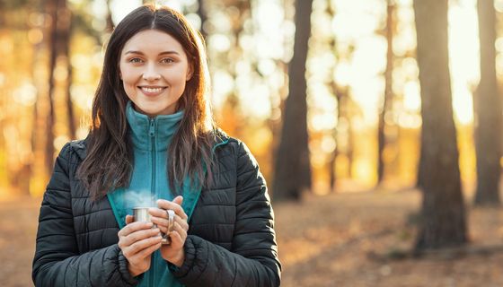 Junge Frau im Wald trinkt eine Tasse dampfenden Tee.