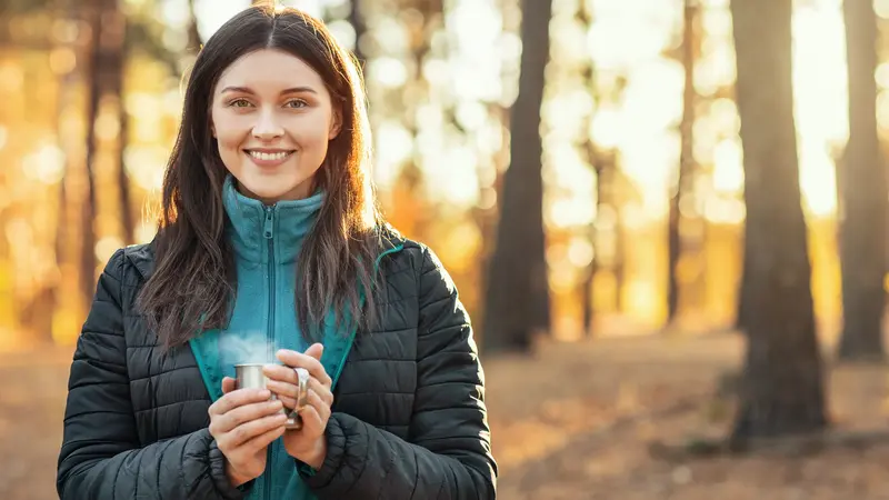 Junge Frau im Wald trinkt eine Tasse dampfenden Tee.