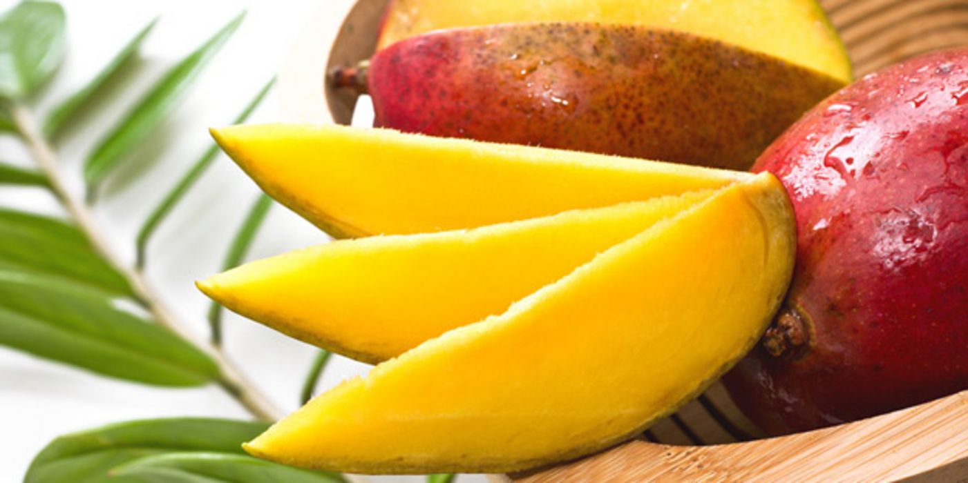 Drei Mangospalten, dahinter eine aufgeschnittene und eine ganze Mango