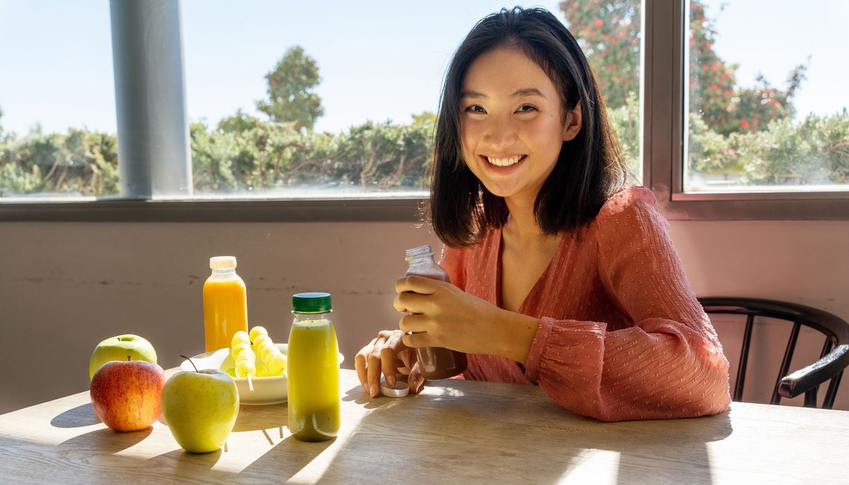 Jugendliches Mädchen sitzt vor Smoothies und Obst.