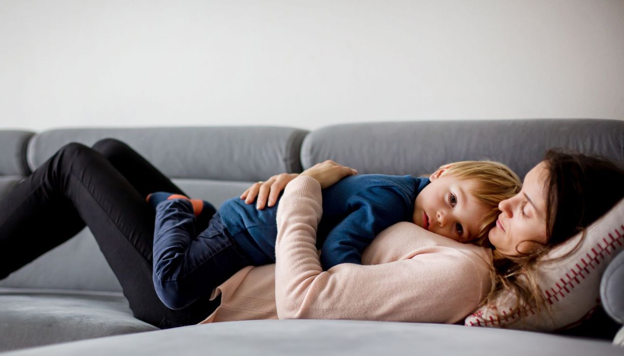 Kleinkind, liegt mit seiner Mutter auf der Couch.