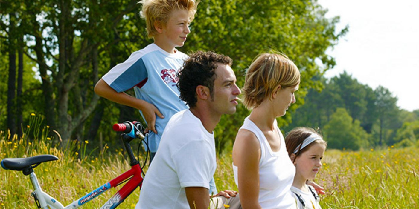 Profile von links, Junge, ca. 10, Vater, Mutter, Tochter, ca. 6, links Jungenfahrrad, Hintergrund sommerliche Natur