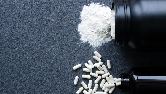 Kreatin als Pulver und Tabletten auf einem dunklen Hintergrund.