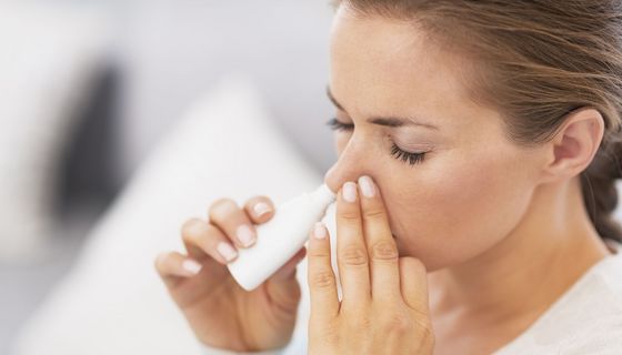 Frau sprüht sich Nasenspray in die Nase.