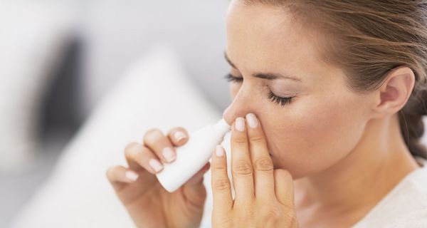 Frau sprüht sich Nasenspray in die Nase.