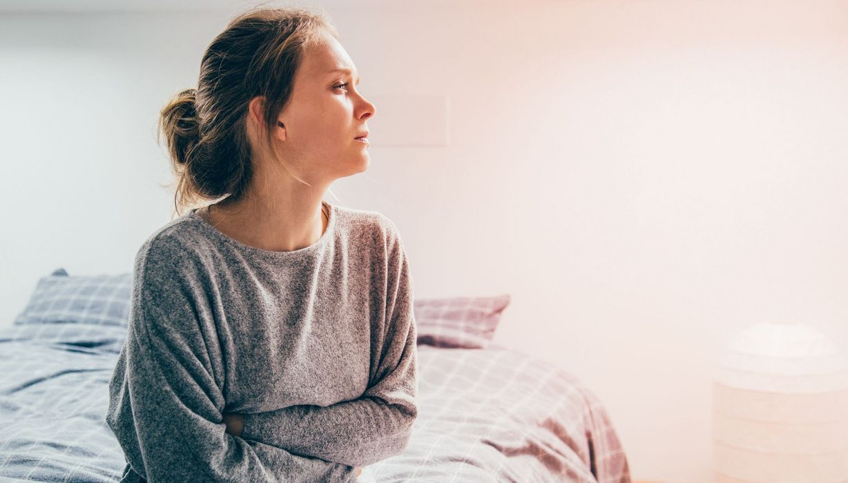 Junge Frau, sitzt im Bett und schaut in die Ferne.