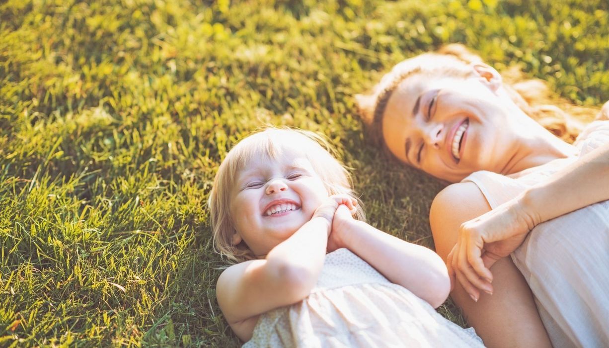 Mutter und Kleinkind liegen vergnügt im Gras.