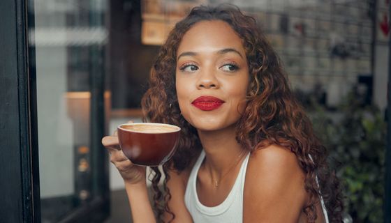 Eine junge Frau trinkt am Fenster Kaffee.