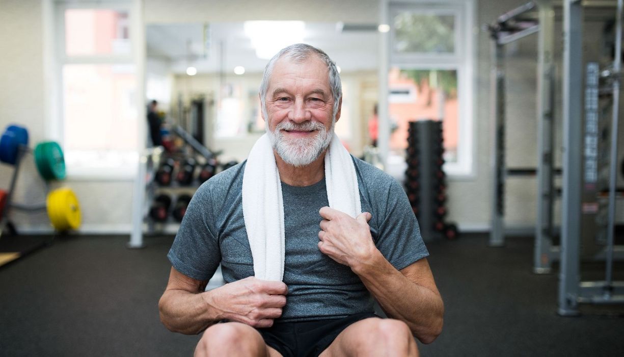 Senior im Fitnessstudio, lächelt in die Kamera.