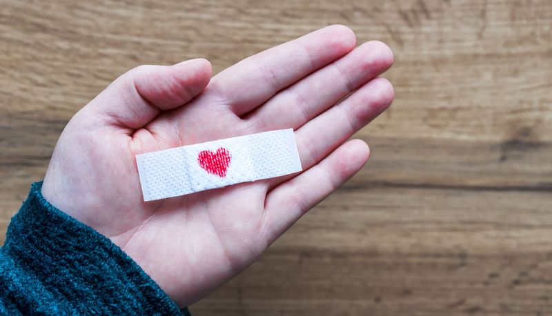 Hand, hält ein Pflaster mit einem roten Herz.