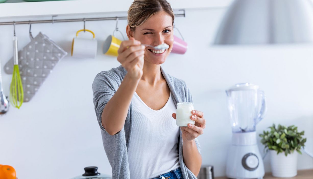 Junge Frau, hält einen Löffel mit Jogurt in die Kamera.