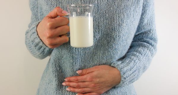 Frau, hält eine Hand an den Bauch und in einer Hand ein Glas Milch.