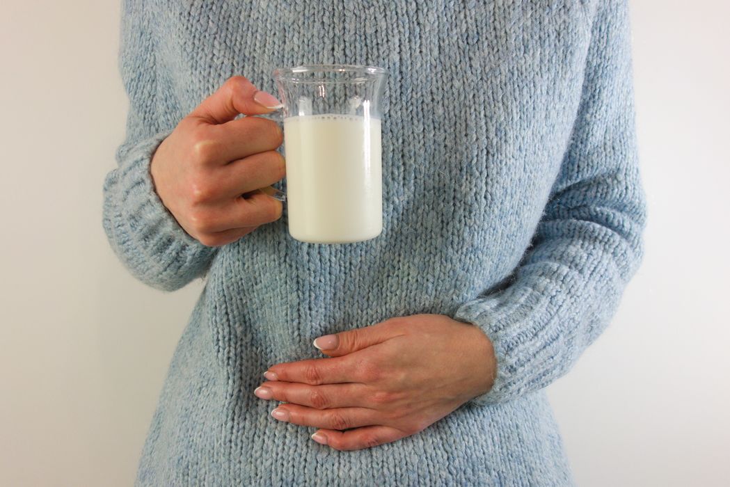 Frau, hält eine Hand an den Bauch und in einer Hand ein Glas Milch.