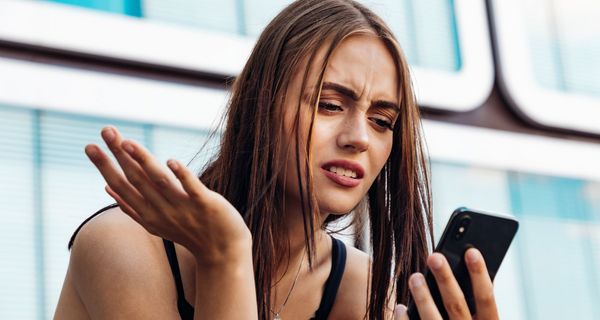 Junge Frau, schaut genervt auf ihr Smartphone.