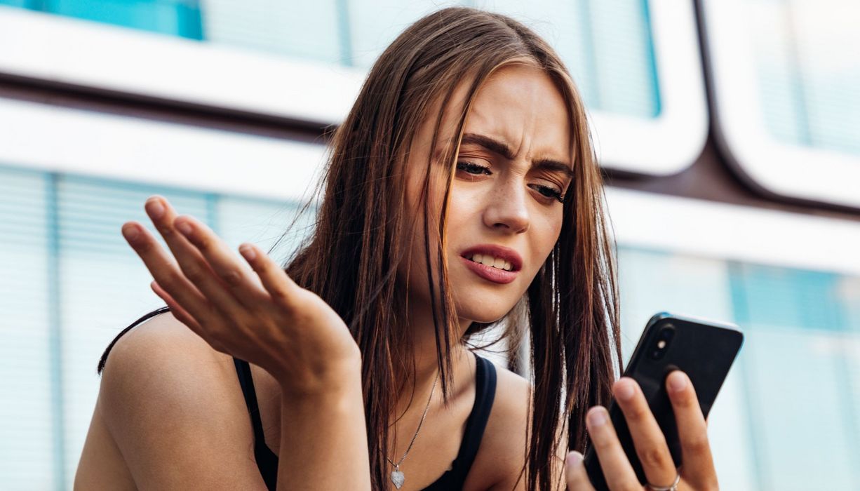 Junge Frau, schaut genervt auf ihr Smartphone.