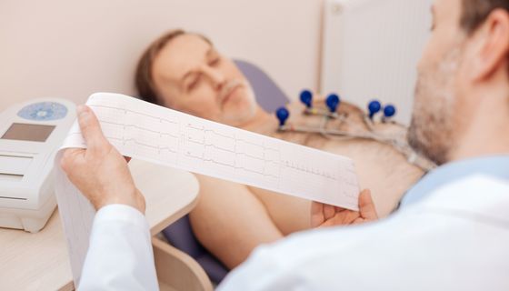 Mann liegt auf einem Krankenhausbett und Arzt liest sein EKG.