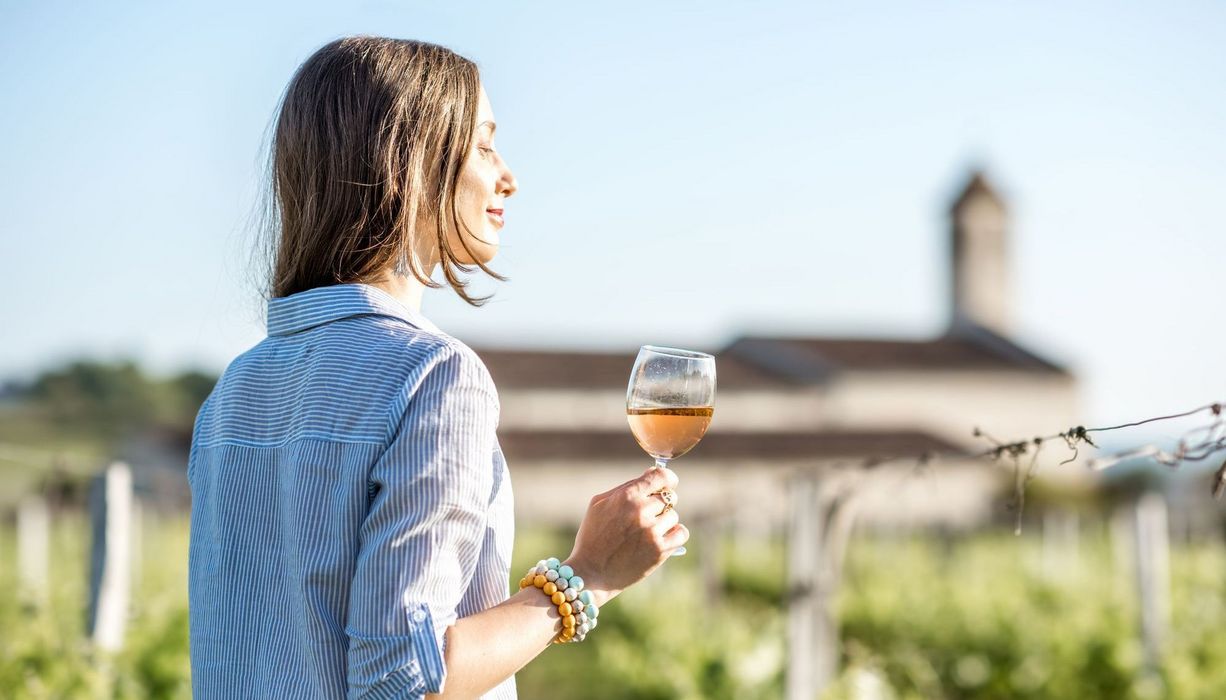 Junge Frau, steht zwischen Weinreben mit einem Glas Wein.