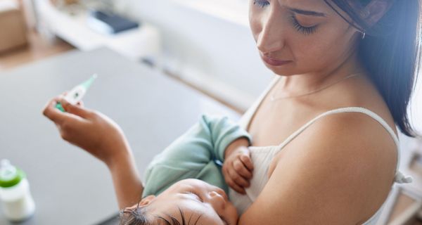 Junge Mutter, hält ihr Baby im Arm und ein Fieberthermometer in der Hand.