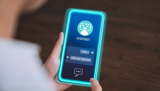 Blick auf ein Smartphone mit einer geöffneten Chatbot-App: Der Bot hat geschrieben: "Hello" und "Can I help you?"