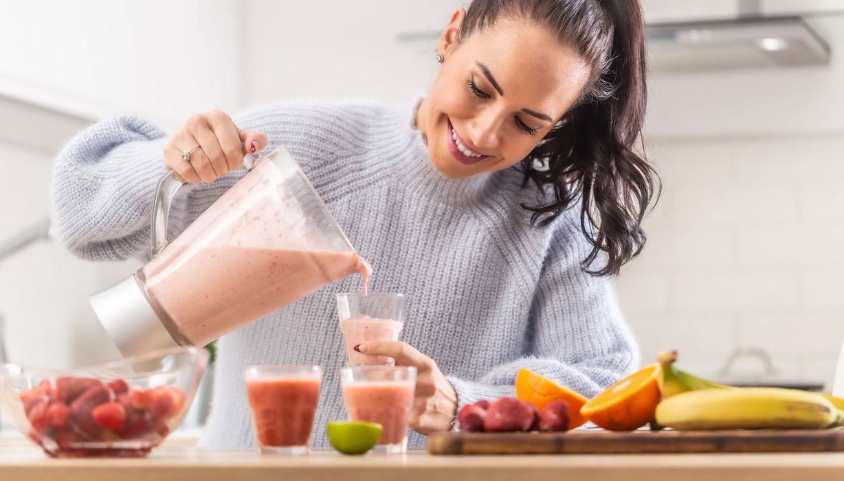 Junge Frau, schenkt sich einen selbstgemachten Smoothie aus einem Mixer ein.