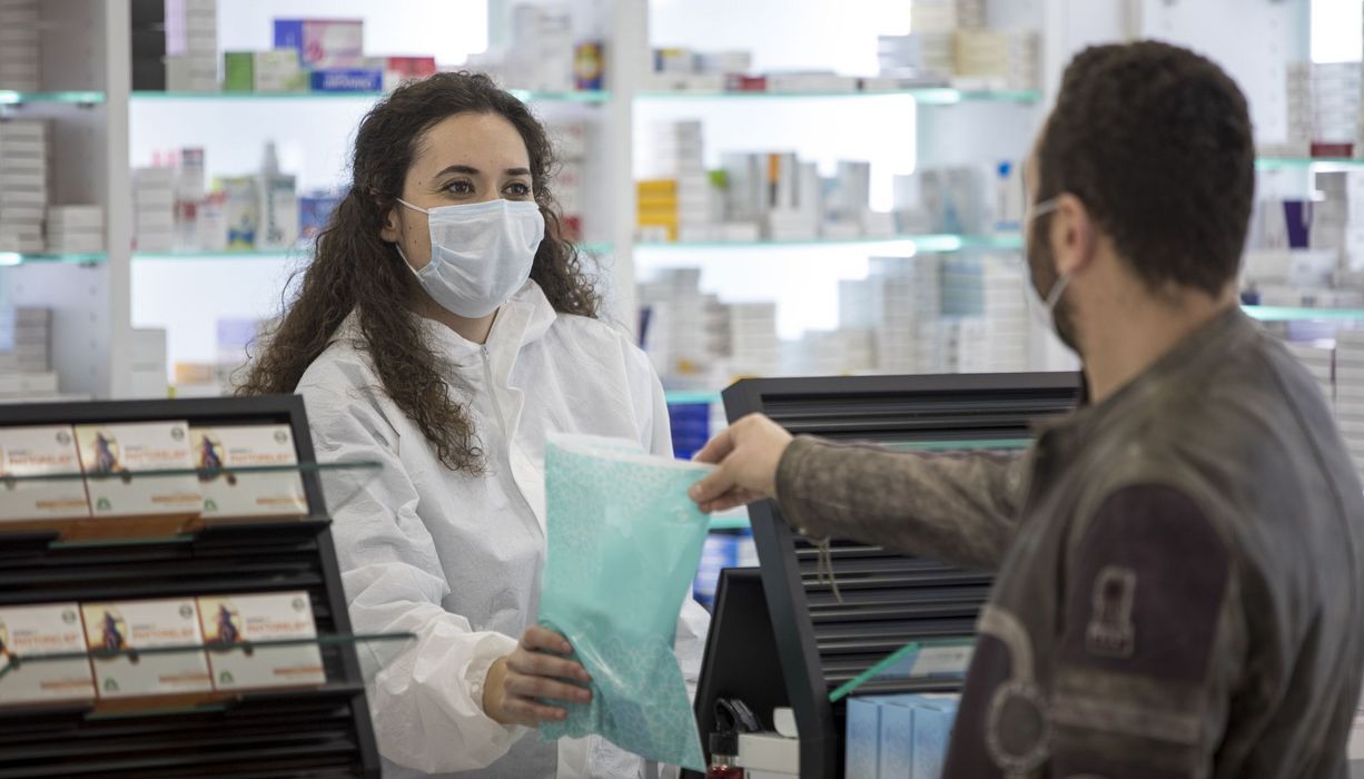 Apothekerin mit Maske übergibt eine Tüte an Patienten.