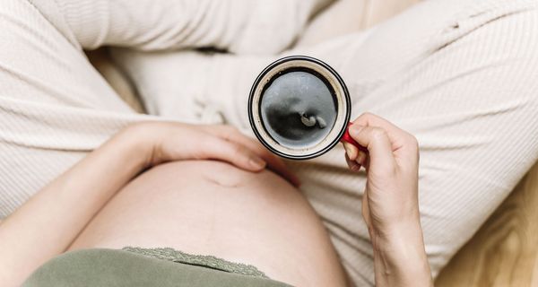 Schwangere Frau, hält eine Tasse Kaffee in der Hand.