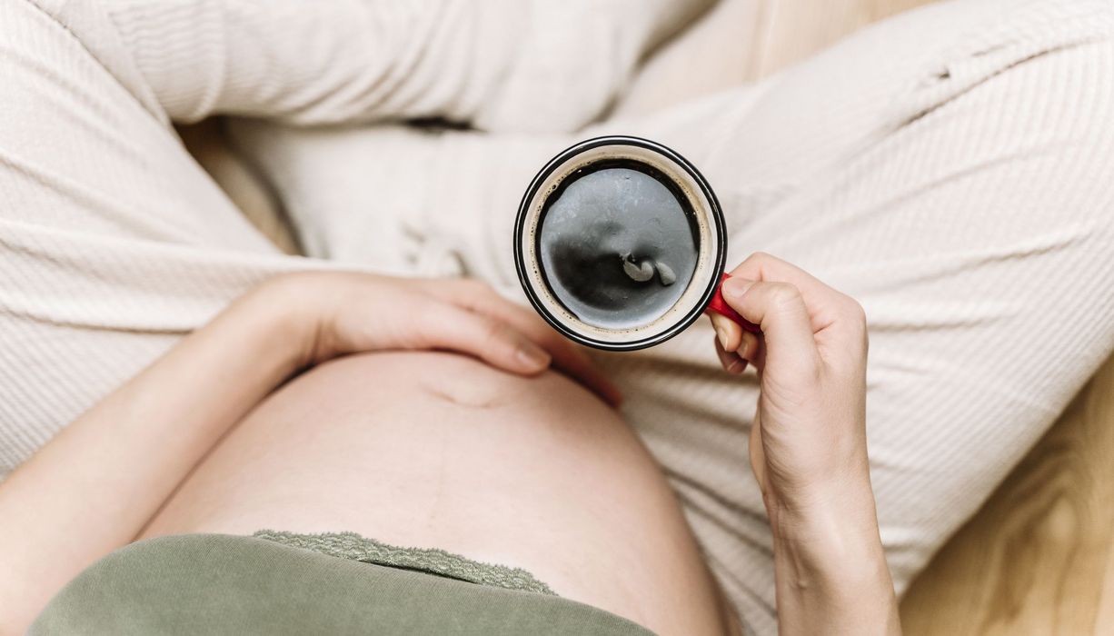 Schwangere Frau, hält eine Tasse Kaffee in der Hand.