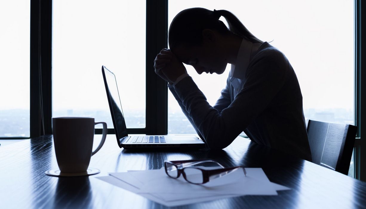 Junge Frau, stützt ihren Kopf auf die Hände und sitzt vor dem Laptop.