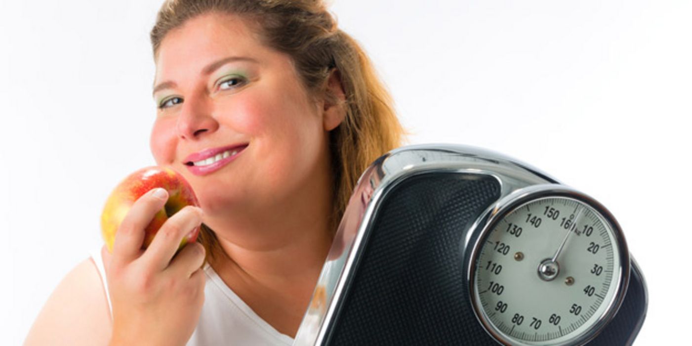 Übergewichtige Frau mit Waage und Apfel in der Hand