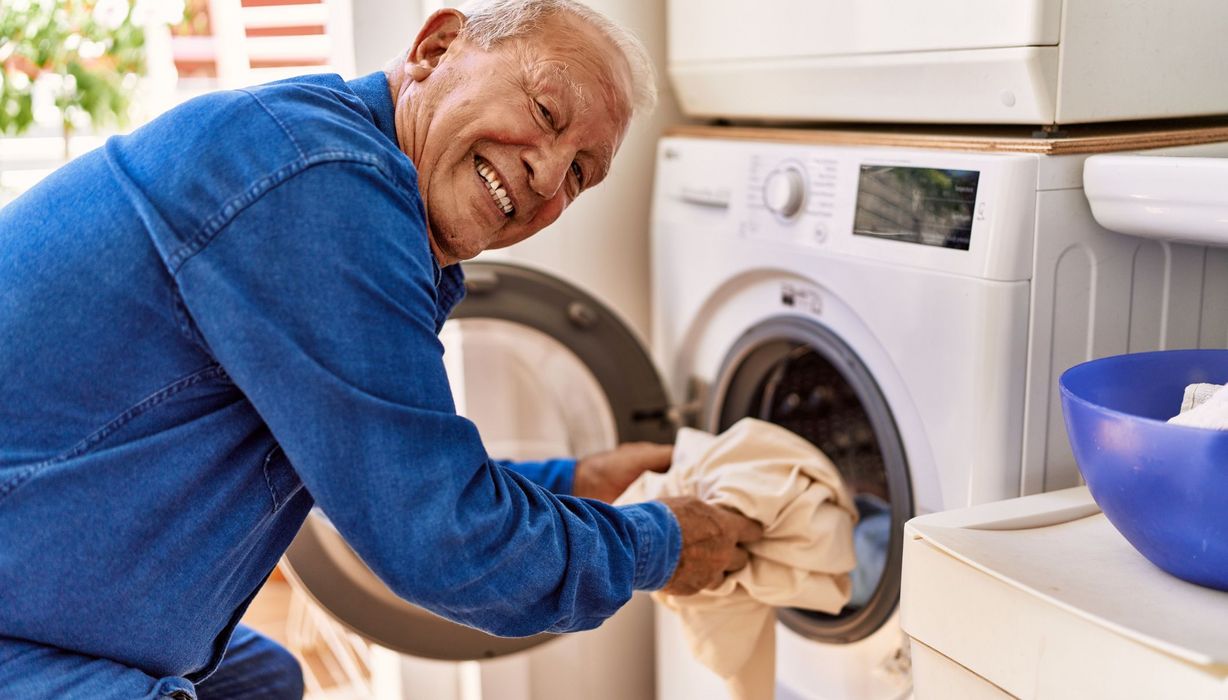 Senior, räumt eine Waschmaschine ein.