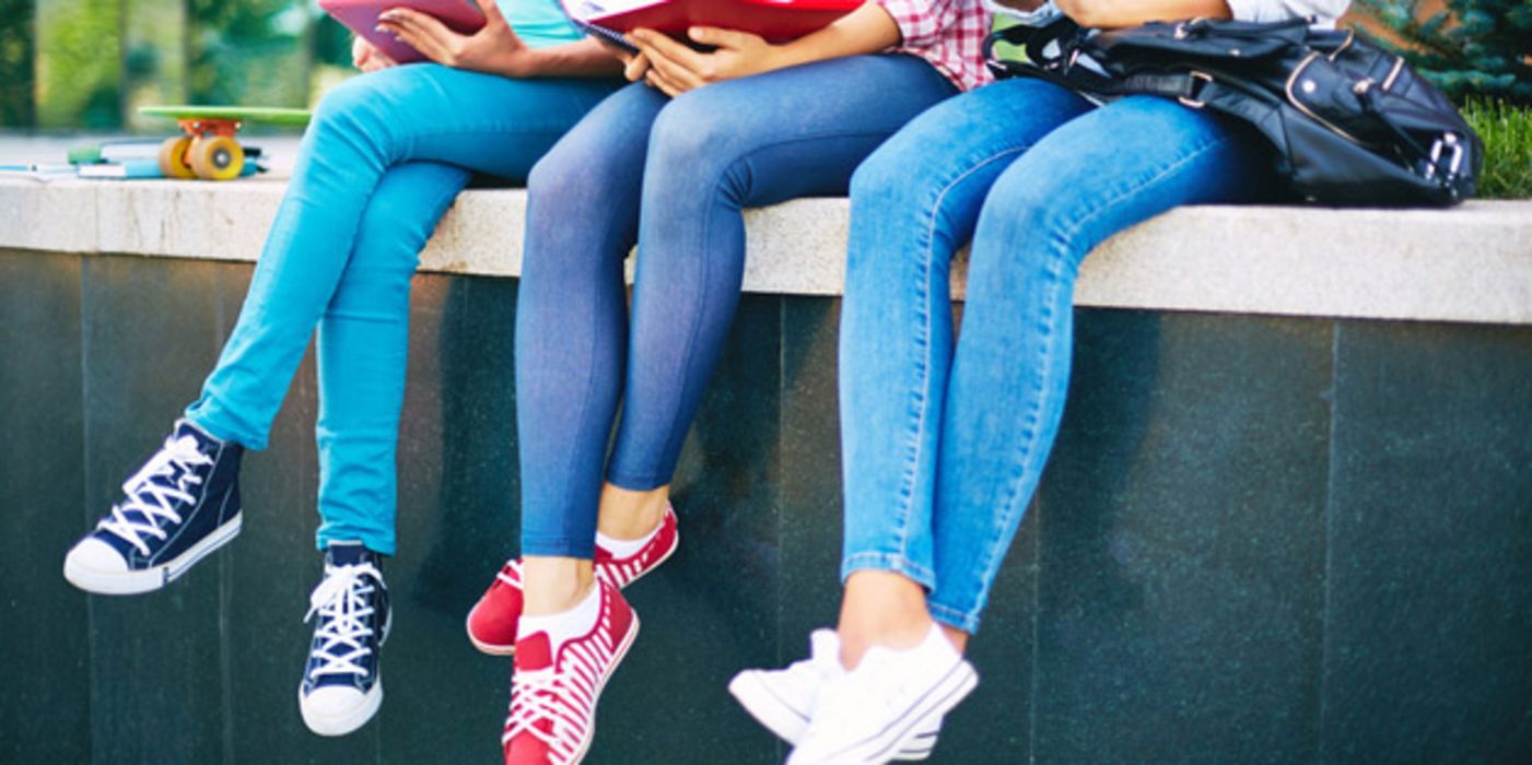 Drei junge, schlanke Frauen sitzen auf einer Mauer, tragen enge Jeans.