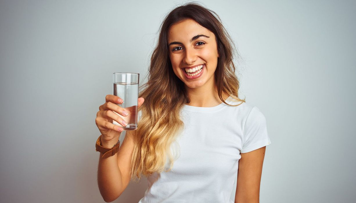 Junge Frau, hält ein Glas Wasser in die Kamera.