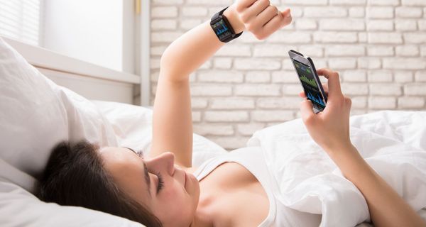 Junge Frau, liegt im Bett und überprüft mit einer Smartwatch ihren Puls.