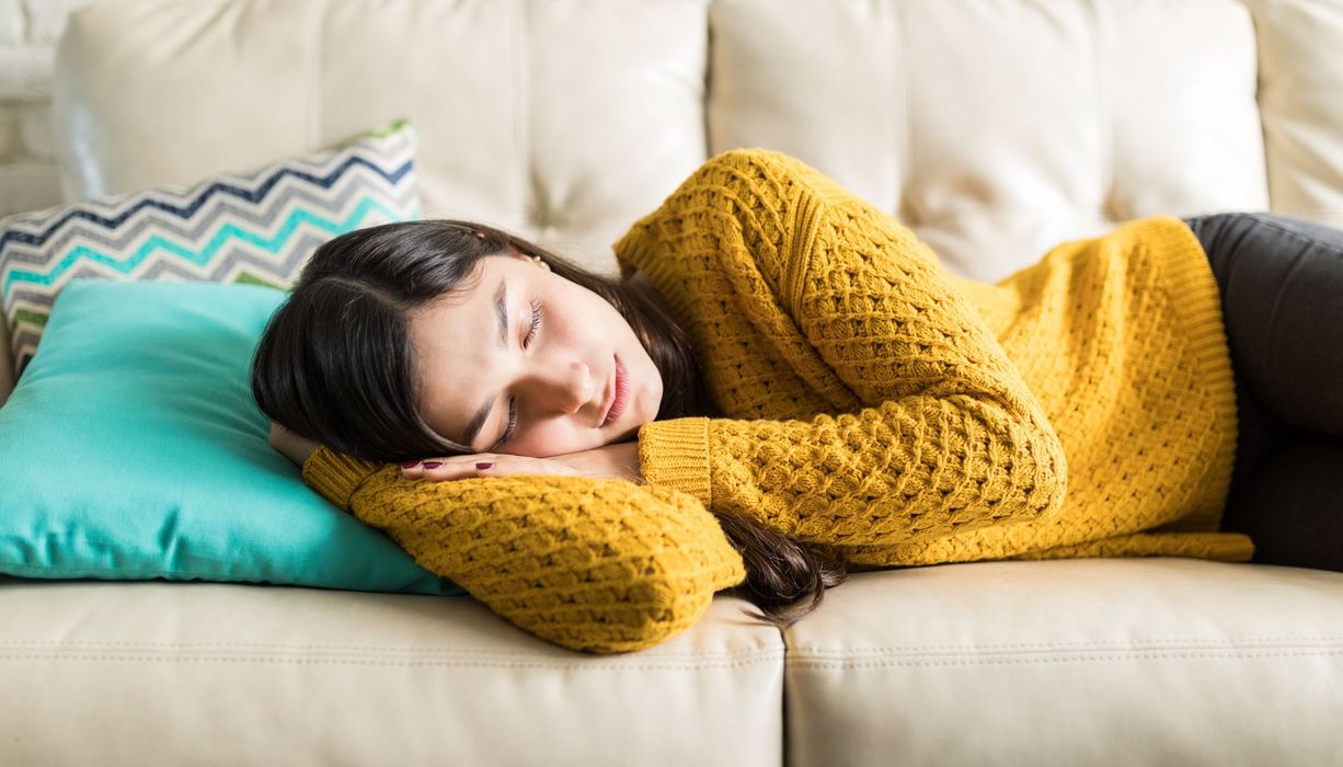 Junge Frau, liegt auf einer Couch und schläft.