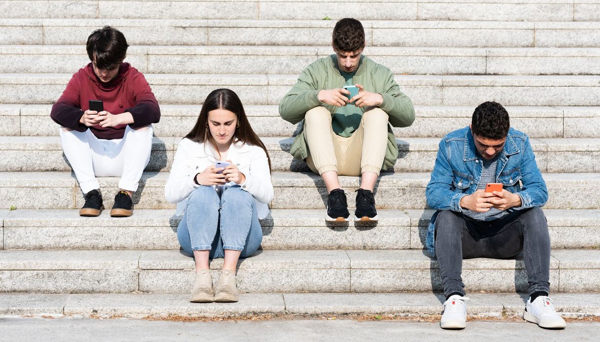 Vier Jugendliche, sitzen auf einer Treppe und schauen auf das Smartphone.