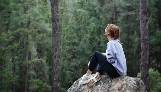 Junge Frau, sitzt auf einem Fels und schaut in den Wald.