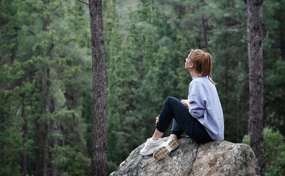 Junge Frau, sitzt auf einem Fels und schaut in den Wald.